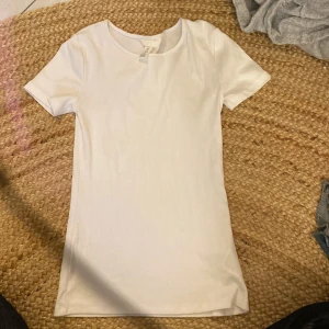 Vit t-shirt - Lång och ribbad vit T-shirt, välldigt ”hudnära” och tight, lång och större halsring. Oanvänd.