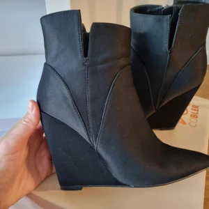 Svarta kilklackade boots - Snygga svarta boots med kilklack och spetsig tå. Dessa boots har en stilren design som passar både till vardags och fest. De är i mycket fint skick och ger en elegant touch till vilken outfit som helst.