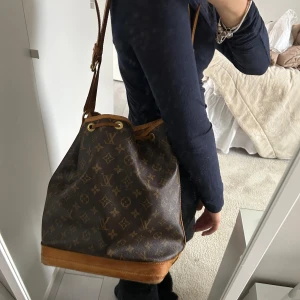 Louis vuitton noe - Säljer en snygg brun axelväska med klassiskt monogrammönster. Väskan har en justerbar axelrem. Den är i acceptabelt skick med lite slitage på botten. Perfekt för vardagsbruk eller en dag på stan!