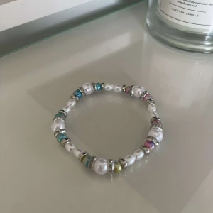 Färgglatt pärlarmband - Säljer ett superfint armband med vita pärlor och färgglada detaljer. Armbandet har en mix av blå, rosa, och gröna pärlor som ger en härlig och livfull känsla. Perfekt för att liva upp vilken outfit som helst!