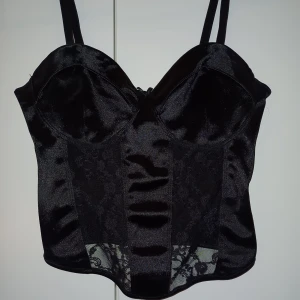 Svart, kort, delvis spetts top - En svart silkesliknande top som har en del spets. Den har använts ett par gånger men passar inte längre. Den är perfekt när man vill klä upp sig men den går även att klä ner med rätt byxor. 