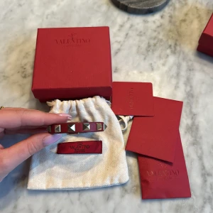 Rött Valentino armband - Rött valentinoarmband med guldiga studs. Armbandet är använt men i jättefint skick. Låda, extra studs och dustbag medföljs. 