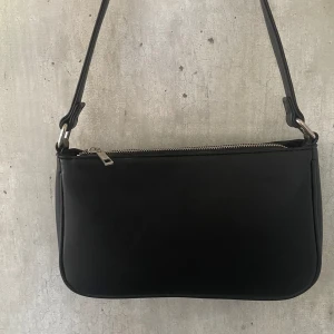 Svart handväska - En vanlig basic, svart handväska med silvrig dragkedja som jag säljer då jag inte använt den alls sen jag köpte den. Nyskick Mått: Bredd 26cm Höjd 15cm