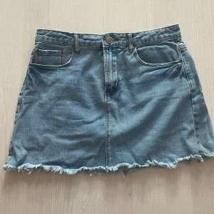 Jeanskjol från Forever 21 - Säljer en snygg jeanskjol från Forever 21 i storlek S. Kjolen har en klassisk blå denimfärg och en rå kant nertill för en cool, avslappnad look. Den har fickor både fram och bak, samt en knapp och dragkedja framtill.