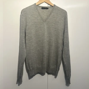 Grå ulltröja från Ralph Lauren - Säljer en stilren och bekväm grå tröja från Ralph Lauren i storlek L. Tröjan är tillverkad i fin merinoull och har en klassisk v-ringad design. Perfekt för både vardag och lite finare tillfällen. Den är långärmad och har ribbade muddar vid ärmslut och nederkant. Passar perfekt till höst- och vintergarderoben!