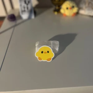 Gul kycklingklistermärke - Ett supersött klistermärke som föreställer en gul kyckling med orange fötter och svartvita ögon. Perfekt för att dekorera din laptop, anteckningsbok eller mobilskal. Klistermärket har en vit kant runt motivet som ger det en fin inramning.
