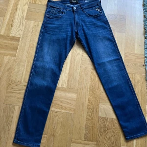Blå jeans från Replay - Säljer ett par snygga blå jeans från Replay anbass. Dom är aldrig använda och säljs pågrund av fel storlek.  Jeansen är i en mörkblå tvätt med lätt slitna detaljer för en cool look. Slim fit