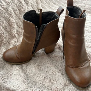 Högklackade boots - Fina högklackade skor i läder material. Lite slitna på utsidan men kan fortfarande användas. Stor i storleken. Passar 38.