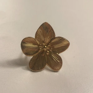 Guldfärgad blomformad ring - Säljer en superfin guldfärgad ring formad som en blomma. Den har detaljerade blomblad som ger en elegant och stilren look. Perfekt för att piffa upp vilken outfit som helst!