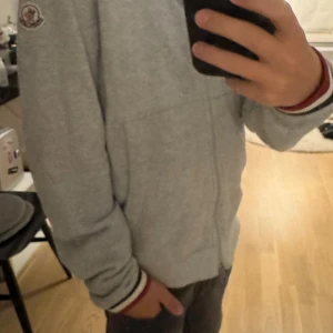 Moncler zip hoodie - Säljer nu denna gråa moncler zip hoodien till ett bra pris! Vid Qr koden har moncler logan lossnat! Skulle ge skicket 9/10 då snörerna saknas vid luvan! Vid snabbt köpt blir det bättre pris!👍🏼☺️🔥