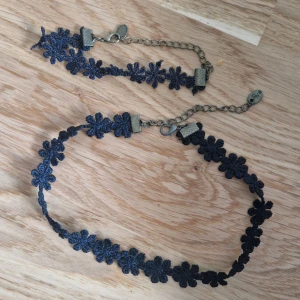 Blommigt smyckesset - Blommig chokerhalsband och armband i svart tyg. Choker ca 41 cm inkl spänne, ca 33 cm exkl spänne. Armband ca 23 cm inkl spänne, ca 13 exkl spänne. 