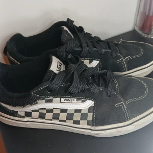 Svarta och vita sneakers från Vans - Säljer ett par klassiska Vans sneakers i svart och vitt med schackrutigt mönster. Skorna har snörning och en bekväm passform. Perfekta för en avslappnad stil.