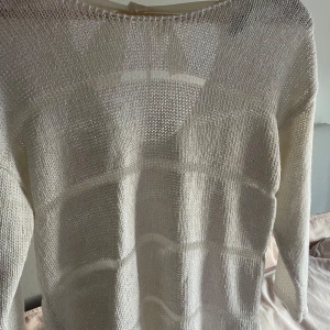 Vit stickad tröja med knytband - Säljer en vit stickad tröja med ett fint knytband i nacken. Tröjan är lite genomskinlig och lite guldig på närhåll.