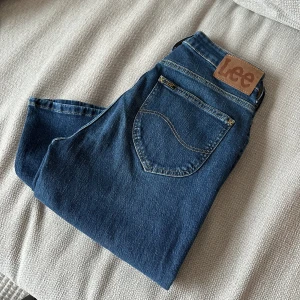 Blå flare jeans från Lee - Snygga blå flare jeans från Lee i storlek 29 i midja. Med klassisk femficksdesign och en bekväm passform. Perfekta för en avslappnad stil. Märkeslogga på bakfickan.