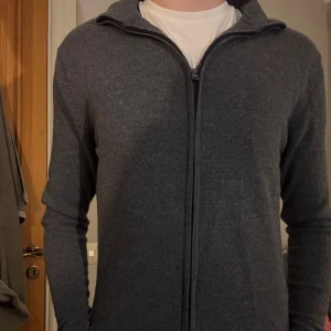 Grå kofta med dragkedja - Säljer en stilren grå kofta med dragkedja. Perfekt för kyligare dagar och enkel att matcha med olika outfits. Koftan har långa ärmar och en hög krage för extra värme. Obs den har krympt i tvätten så den sitter mer som en S istället för en M nu men annars är den fortfarande i bra skick och är helt ny👍 (Är 182 cm lång)