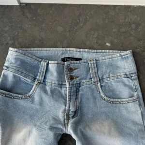 Ljusblå jeans med nitar från Zulu - Snygga ljusblå jeans  med nitar på fickorna. De har en bootcut-stil och två knappar i midjan. Perfekta för en avslappnad look. Midjemått 42 rakt över!!🥰