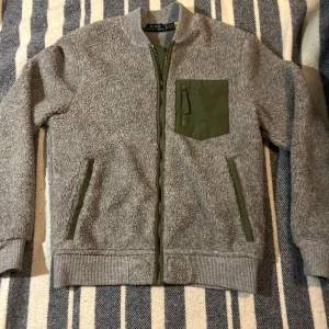 Grå fleece från Ralph Lauren - Säljer en snygg grå fleece från Ralph Lauren med gröna detaljer. Jackan har en dragkedja framtill och en praktisk bröstficka med dragkedja. Perfekt för kyliga dagar! Storleken är Xs men passar även S bra! Ifall du har några funderingar är det bara att höra av sig!👀👀