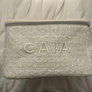 Vit necessär från CAIA - Snygg vit necessär från CAIA med ett quiltat mönster och praktiskt handtag. Perfekt för att organisera dina skönhetsprodukter. Den har en dragkedja för säker förvaring. Julkalender 2022.
