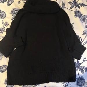 Svart stickad polotröja - Mysig svart stickad polotröja med en hög krage och trekvartsärmar. Perfekt för kyliga dagar och ger en avslappnad look. Tröjan har en loose passform som gör den bekväm att bära.