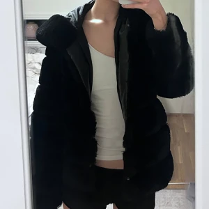 Svart pälsjacka med huva - Säljer en svart pälsjacka med huva. Perfekt inför vintern och extremt mysig. Den passar även bra inför utekvällar då den är väldigt stilren. Jackan har ett litet hål i insidan av ärmen, men det är inget jag själv stört mig på, och syns inte alls❤️