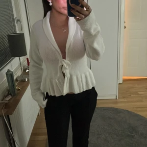 Vit ribbad kofta med knyt - Snygg vit ribbad kofta med knyt framtill och volangdetaljer i nederkant. Perfekt för en stilren look. Tröjan är helt ny med prislapp