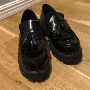 Svarta loafers från Vagabond - Snygga svarta loafers från Vagabond med dekorativa tofsar på ovansidan. Skorna har en robust sula och är tillverkade i blankt syntetmaterial. Perfekta för en stilren look. Skorna är sparsamt använda och i ett mycket gott skick! 