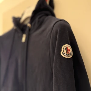 Moncler Magila full zip hoddie navy - Hej. Säljer nu denna snygga Moncler hoddie för jag inte använder den då jag växt ut ur den. Köpte den för 3 år sedan för 5099kr. Har bara använts på speciella tillfällen  man får med sig påsen men har tyvär tappat bort kvitto.  det är bara och göra av sig om det är något.