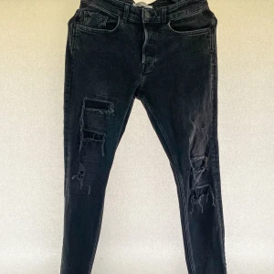 ZARA distressed jeans - Snygga svarta jeans från Zara med trendiga slitningar på framsidan. De har en knappstängning och är tillverkade i ett bekvämt material som ger en tight passform. Storlek: 40 EUR.  Hör av er vid eventuella frågor!!