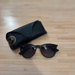 Svarta solglasögon från Ray-Ban - Snygga svarta solglasögon från Ray-Ban med klassisk design. De har en stilren svart båge och mörka linser som ger ett coolt och tidlöst intryck. Perfekta för soliga dagar och kommer med ett matchande svart fodral.