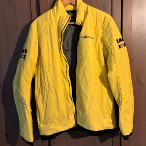 Gul jacka från Sail Racing - Snygg gul jacka från Sail Racing med dragkedja och logga på bröstet. Jackan är tillverkad i nylon och polyester, perfekt för kyligare dagar. Den har långa ärmar och en stilren design. Köpt för 2500, använd fåtal gånger