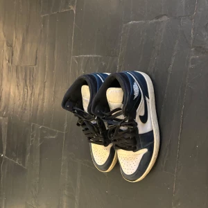 Nike air Jordan 1 mid - Snygga Nike Air Jordans i en stilren kombination av blått och vitt. Skorna har klassisk snörning och en ikonisk design med Nike-loggan på sidan. Jordan mid naivy 