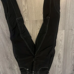 Ridbyxor - Snygga svarta byxor med kontrasterande vita sömmar. Byxorna har en tight passform och är perfekta för en stilren look. De har praktiska fickor och en bekväm midja.
