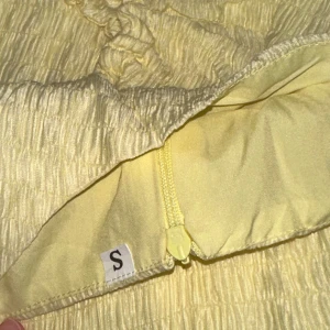 Gul klänning - Säljer en snygg gul klänning med en unik design. Klänningen har en öppning på båda sidor och en slits framtill som ger en elegant touch. Materialet är lätt och luftigt, perfekt för varmare dagar. Passar perfekt för sommarens alla tillfällen!