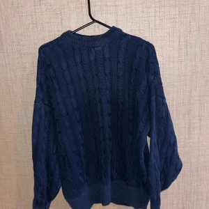 Mörkblå stickad tröja - Säljer en mysig mörkblå stickad tröja med kabelstickat mönster. Tröjan har långa ärmar och en rund halsringning. 