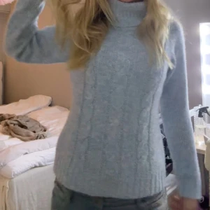 Ljusblå stickad polotröja - Säljer en mysig ljusblå stickad polotröja med kabelstickat mönster. Tröjan har långa ärmar och en hög polokrage som håller dig varm under kyliga dagar. Perfekt för höst och vinter!