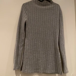 Grå ribbad polotröja - Säljer en stilren grå ribbad polotröja med långa ärmar. Perfekt för kyligare dagar och enkel att matcha med olika outfits. Ett måste i garderoben för den som gillar klassiska plagg.