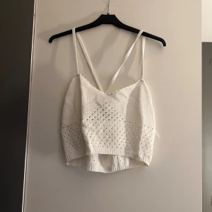 Vit stickad linnetopp - Säljer en söt vit stickad linnetopp med smala axelband och korsad rygg. Perfekt för varma sommardagar eller som ett lager under en jacka. Toppen har en fin struktur och är lätt att matcha med olika outfits.
