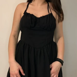 Svart klänning med smala axelband - Snygg svart klänning med smala axelband och en åtsittande överdel som ger en fin siluett. Kjolen är lätt utställd vilket ger en luftig känsla. Perfekt för en stilren look.