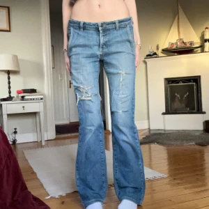 Blå bootcut jeans med slitningar - Snygga blå bootcut jeans med coola slitningar på framsidan. Hålet under ena fickan har tyg under sig, se sista bilden!
