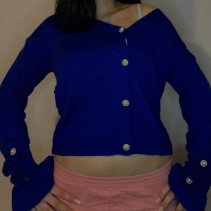 Blå ribbad kofta med knappar - Snygg blå kofta med ribbade detaljer och knappar framtill. Den är croppad och har långa ärmar med knappar vid ärmsluten. Perfekt för en stilren look.