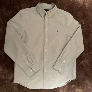 Blå skjorta från Ralph Lauren - Riktigt stilig blå Polo Ralph Lauren skjorta. Storleken är 14-16 år och är använd fåtal gånger. Kom privat vid minsta lilla fundering. 