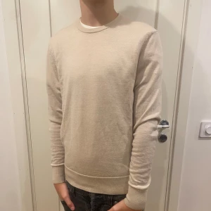Beige stickad tröja - Säljer en stilren beige långärmad tröja med rund hals. Perfekt för en avslappnad look. Tröjan har ribbade muddar vid ärmslut och nederkant för en snygg passform. Den är i 100% merinoull  storlek xs modellen är 177 tröjan är använd ett fåtal gånger