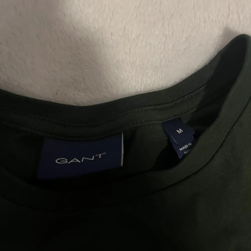 Säljer en stilren grön t-shirt från GANT med liten broderad logga på bröstet. Perfekt för en avslappnad look. T-shirten är kortärmad och gjord i mjukt material.. T-paidat.