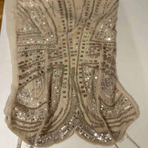 Beige klänning med paljetter - Säljer en elegant beige klänning dekorerad med glittrande paljetter i ett detaljerat mönster. Perfekt för en utekväll eller en fin middag Klänningen har en figurnära passform och är tillverkad i ett mjukt material.