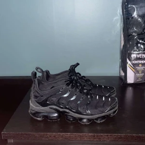 Vapormax skor  - Snygga svarta sneakers med snörning och en unik sula. Perfekta för en sportig look. De har en diskret design med små vita detaljer och en bekväm passform.