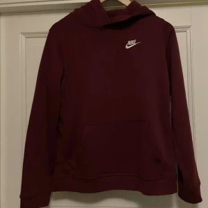 Vinröd hoodie från Nike - Säljer en snygg vinröd hoodie från Nike med klassisk logga på bröstet. Tröjan har en bekväm passform med långa ärmar och en praktisk magficka. Perfekt för kyligare dagar.