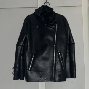 Skinnjacka från CHAMMAS STOCKHOLM (nyskick aldrig använt)  - Säljer denna fina skinnjacka pga passar inte mig. Aldrig använd och i toppskick! Jag är 167 lång normalbyggd. Upplever att den är normal i storlek. Jag har lite större byst därför kan den upplevas lite tightare på mig. Gillar den skarpt, snygg design med spännen vid hals och ärmar, men skinnjackor passar helt enkelt inte mig. Veganskt läder 100% polyester. Köptes för 1500 kr. PRIS KAN DISKUTERAS :)