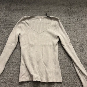 Beige ribbad tröja från H&M - Säljer en stilren beige ribbad tröja från H&M. Tröjan har en v-ringad hals och långa ärmar, perfekt för en elegant och avslappnad look. Passar bra till både jeans och kjol. Den är stickad. 