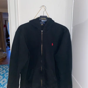 Svart hoodie från Ralph Lauren - Säljer en klassisk svart hoodie från Ralph Lauren med dragkedja. Perfekt för en stilren och bekväm look. öppen till prisförslag!