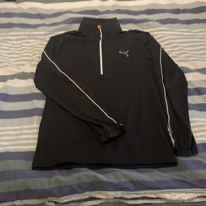 Svart långärmad tröja från Puma - Snygg svart långärmad tröja från Puma med dragkedja och vit logga på bröstet. Tröjan har vita detaljer längs ärmarna och en hög krage. Perfekt för träning eller en avslappnad dag. Pris går alltid att förhandlas.